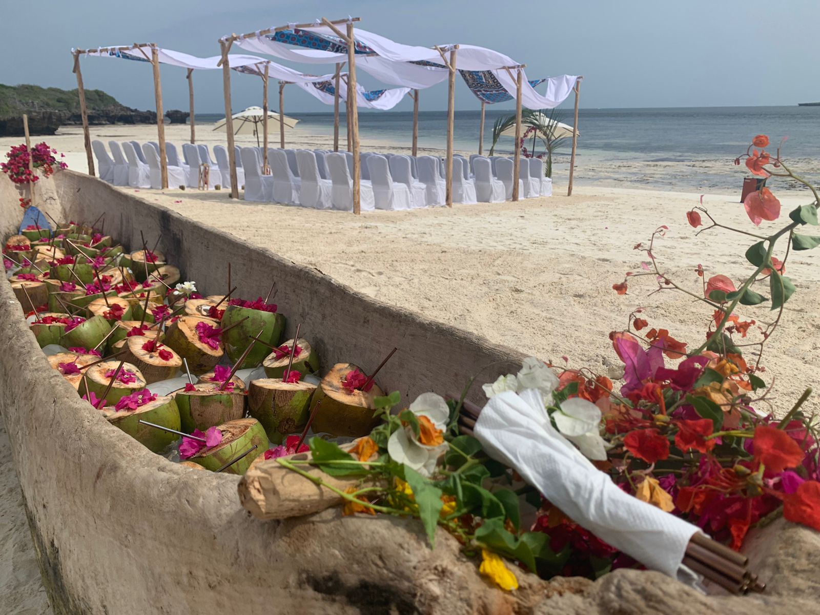 Ein mit frischen Kokosnüssen gefülltes Holzboot als Empfang für eine Hochzeit in Kenia am weißen Sandstrand, mit Blick auf den Traubogen am Meer – tropische Inspiration für die Hochzeitsplanung und das traumhafte Heiraten in Kenia.