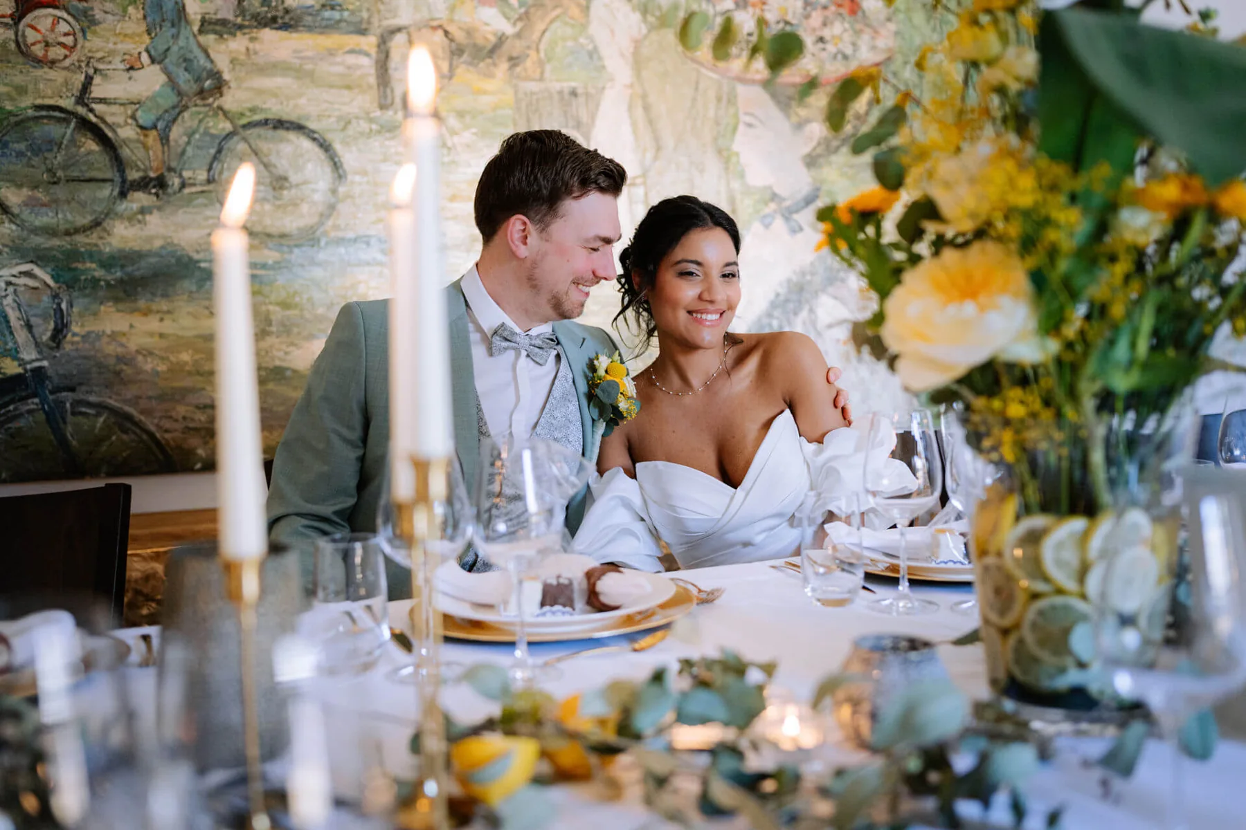 Brautpaar an einer festlich gedeckten Hochzeitstafel mit Kerzen und Blumen.