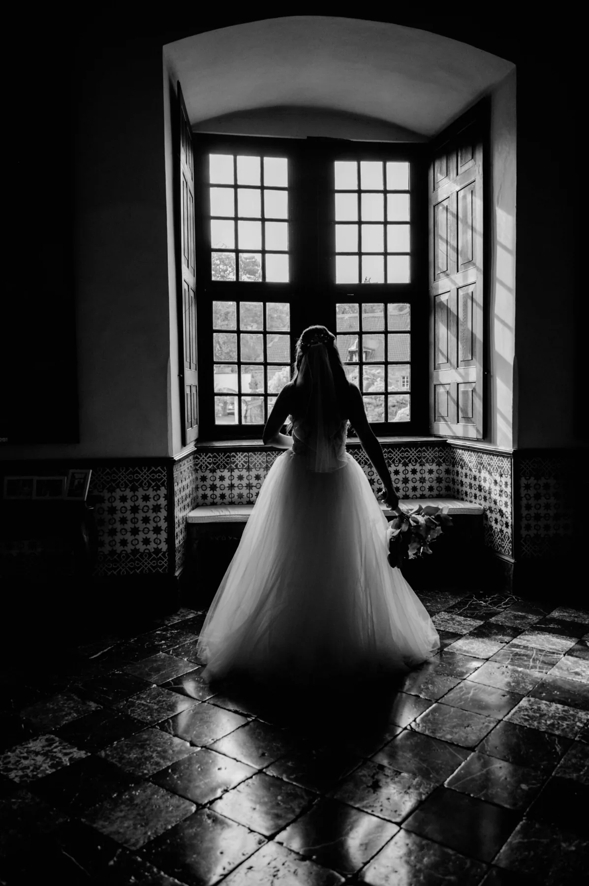 Braut im Hochzeitskleid vor einem Fenster in Schwarz-Weiß